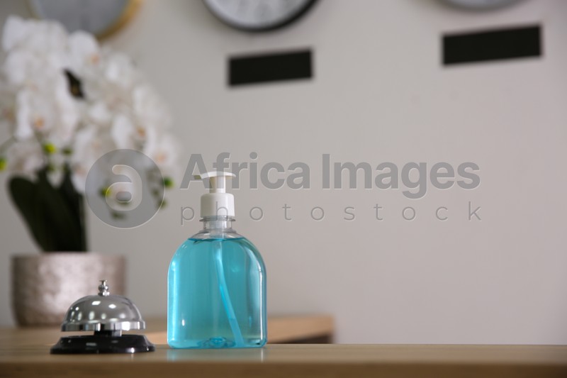 Photo of Dispenser bottle of antiseptic gel and service bell on reception desk in hotel. Space for text