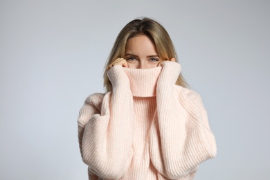 Beautiful young woman wearing knitted sweater on light grey background