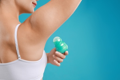 Young woman applying deodorant to armpit on teal background, closeup