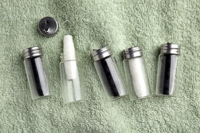 Biodegradable dental flosses in glass jars on light green towel, flat lay
