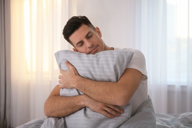 Man hugging pillow on bed with grey linens at home