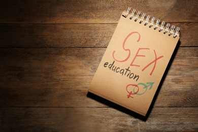 Notebook with phrase "SEX EDUCATION" and gender symbols on wooden background, top view. Space for text