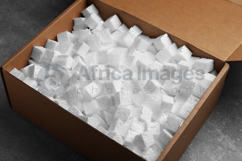 Cardboard box filled with polystyrene styrofoam pieces on grey table, closeup