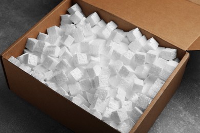 Cardboard box filled with polystyrene styrofoam pieces on grey table, closeup