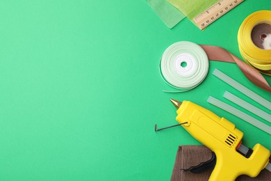 Photo of Hot glue gun and handicraft materials on green background, flat lay. Space for text