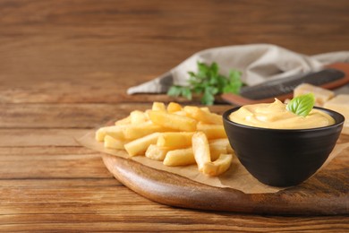 Delicious French fries and cheese sauce with basil on wooden table, space for text