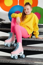 Cute indie girl with roller skates sitting on stairs indoors