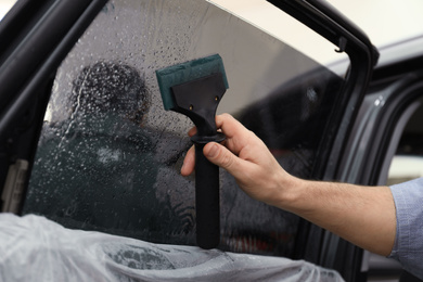 Worker washing tinted car window in workshop, closeup