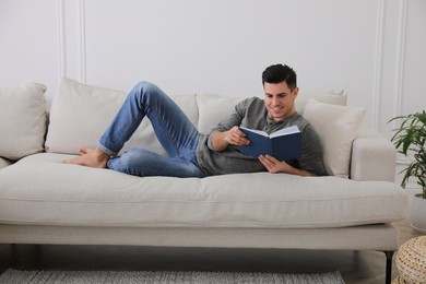 Man with book lying on comfortable sofa in living room