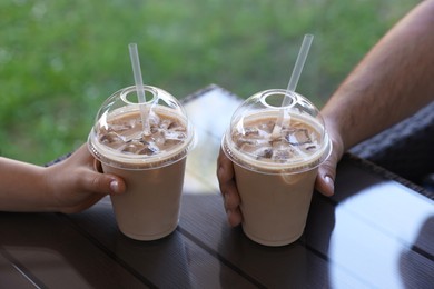 Man and woman with plastic takeaway cups of delicious iced coffee at table in outdoor cafe, closeup