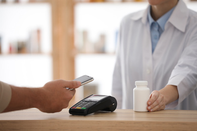 Customer using terminal for contactless payment with smartphone in pharmacy, closeup