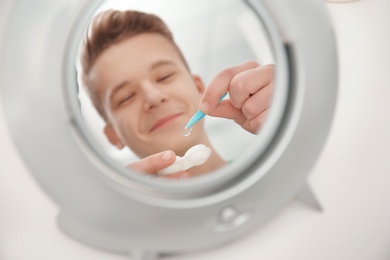 Mirror reflection of teenage boy taking contact lens from container