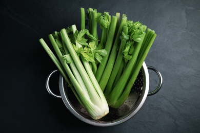 Fresh green celery in colander on black table, top view