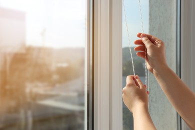 Woman opening blinds on window indoors, closeup. Space for text