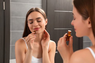 Photo of Young woman smelling essential oil in bathroom