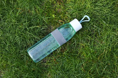 Photo of Glass bottle of fresh water on green grass outdoors, top view