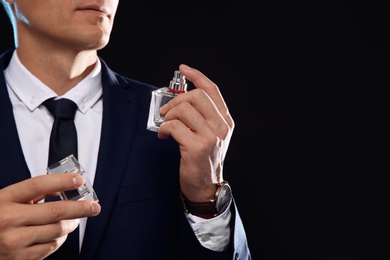 Young man with perfume bottle on black background, closeup. Space for text