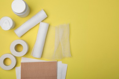 White bandage rolls and medical supplies on yellow background, flat lay. Space for text