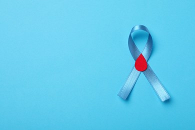 Photo of Light blue ribbon with paper blood drop on color background, top view and space for text. Diabetes awareness