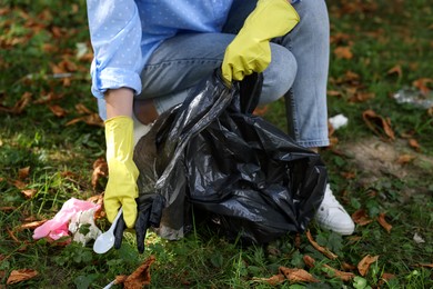 Photo of Woman with plastic bag collecting garbage in park, closeup