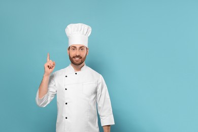 Photo of Smiling mature chef showing idea gesture on light blue background, space for text