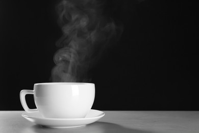 Cup with steam on table against black background. Space for text
