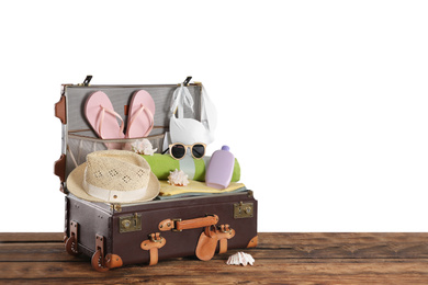 Open vintage suitcase with different beach objects packed for summer vacation on wooden table against white background