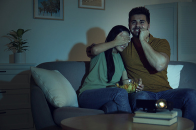 Emotional young couple watching movie using video projector at home