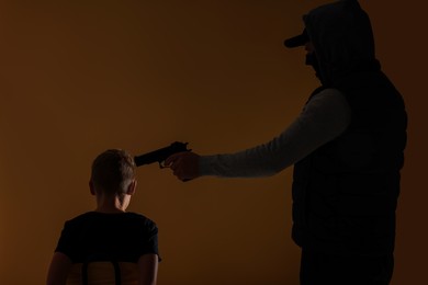 Photo of Kidnapper pointing gun at little boy taken hostage on dark background
