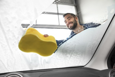 Worker cleaning automobile windshield with sponge at car wash, view from inside