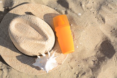 Stylish straw hat, sea shell and sunscreen on sandy beach, top view