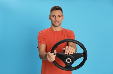 Happy man with steering wheel on light blue background. Space for text