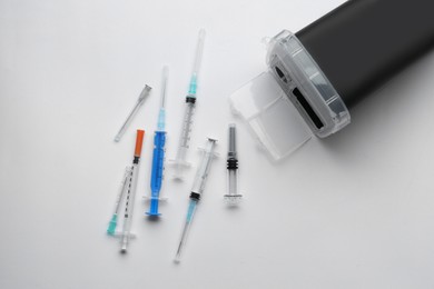 Disposable syringes with needles and sharps container on white background, top view