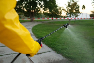 Person in hazmat suit disinfecting street with sprayer, closeup. Surface treatment during coronavirus pandemic
