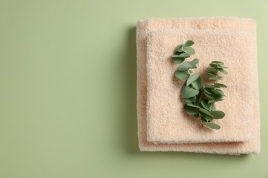 Soft folded towels with eucalyptus branch on green background, top view. Space for text