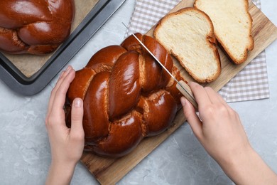 Woman cutting homemade braided bread at grey table, top view. Traditional Shabbat challah
