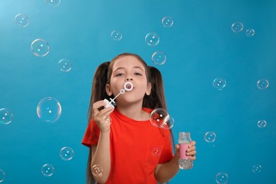 Little girl blowing soap bubbles on light blue background