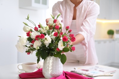Woman with bouquet of fresh flowers in stylish vase at table, closeup