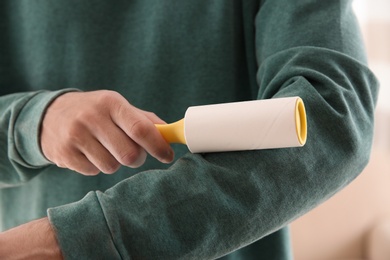 Photo of Man cleaning green sweatshirt with lint roller on light background, closeup