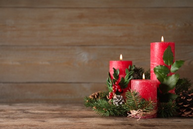 Burning red candles with Christmas decor on wooden table. Space for text