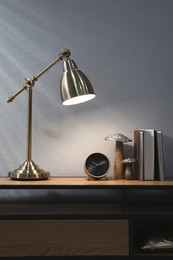 Stylish lamp, clock and books on wooden cabinet indoors. Interior design