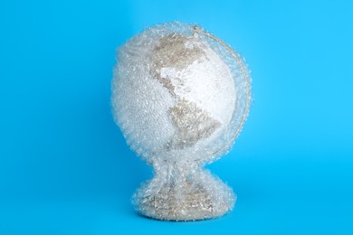 Globe packed in bubble wrap on turquoise background. Environmental conservation