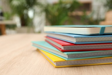 Stack of colorful planners on wooden table indoors, closeup. Space for text