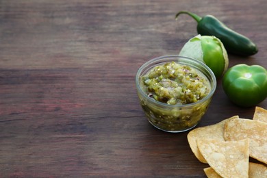Photo of Tasty salsa sauce, ingredients and tortilla chips on wooden table, space for text