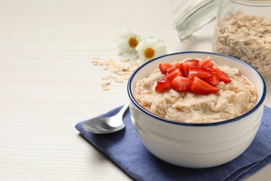 Tasty oatmeal porridge with strawberries served on white wooden table. Space for text