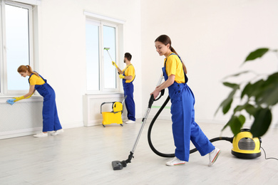 Team of professional janitors in uniforms cleaning room