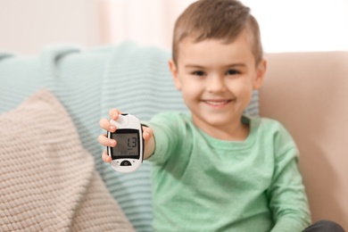 Little boy holding digital glucose meter at home, focus on hand. Diabetes control