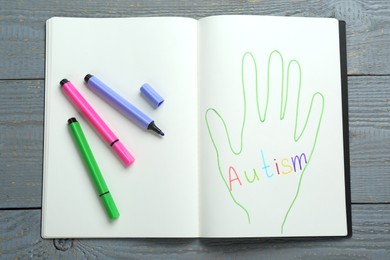 Colorful felt tip pens and notebook with word Autism on grey wooden table, top view
