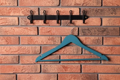 Hook rack with blue clothes hanger on red brick wall