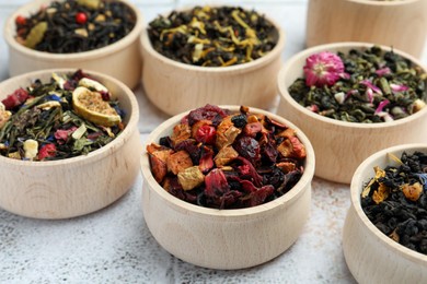 Photo of Different kinds of dry herbal tea in wooden bowls on white tiled surface